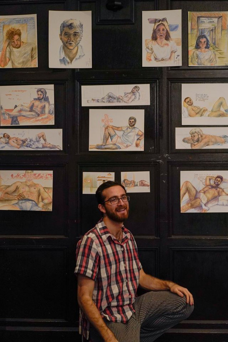 Kaan Tarhan stands poses in front of his series of portraits, titled "Chat & Sketch."